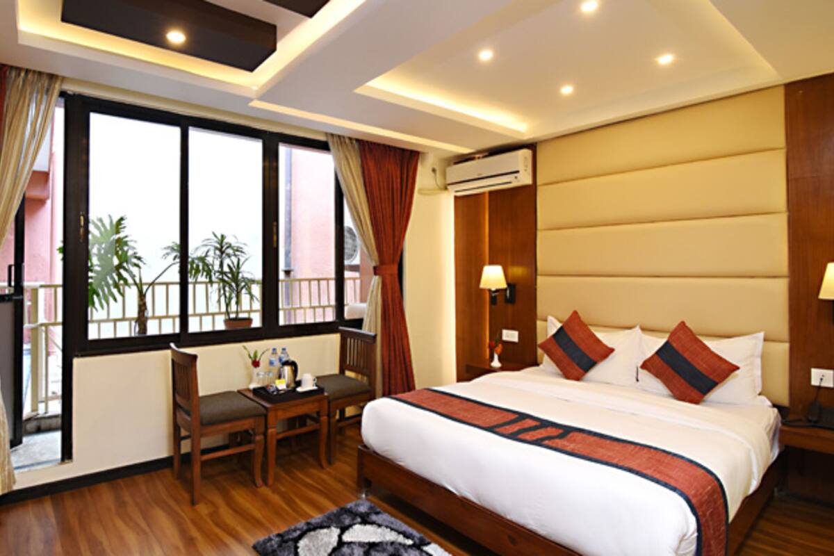 A hotel room with a large bed, a desk with a computer, a chair, and a view of palm trees through the window.