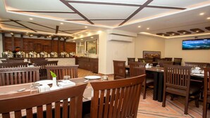 A restaurant with wooden furniture, a TV mounted on the wall, and a kitchen area with stainless steel appliances. - MeroStay 172 Hotel JP (Kathmandu)