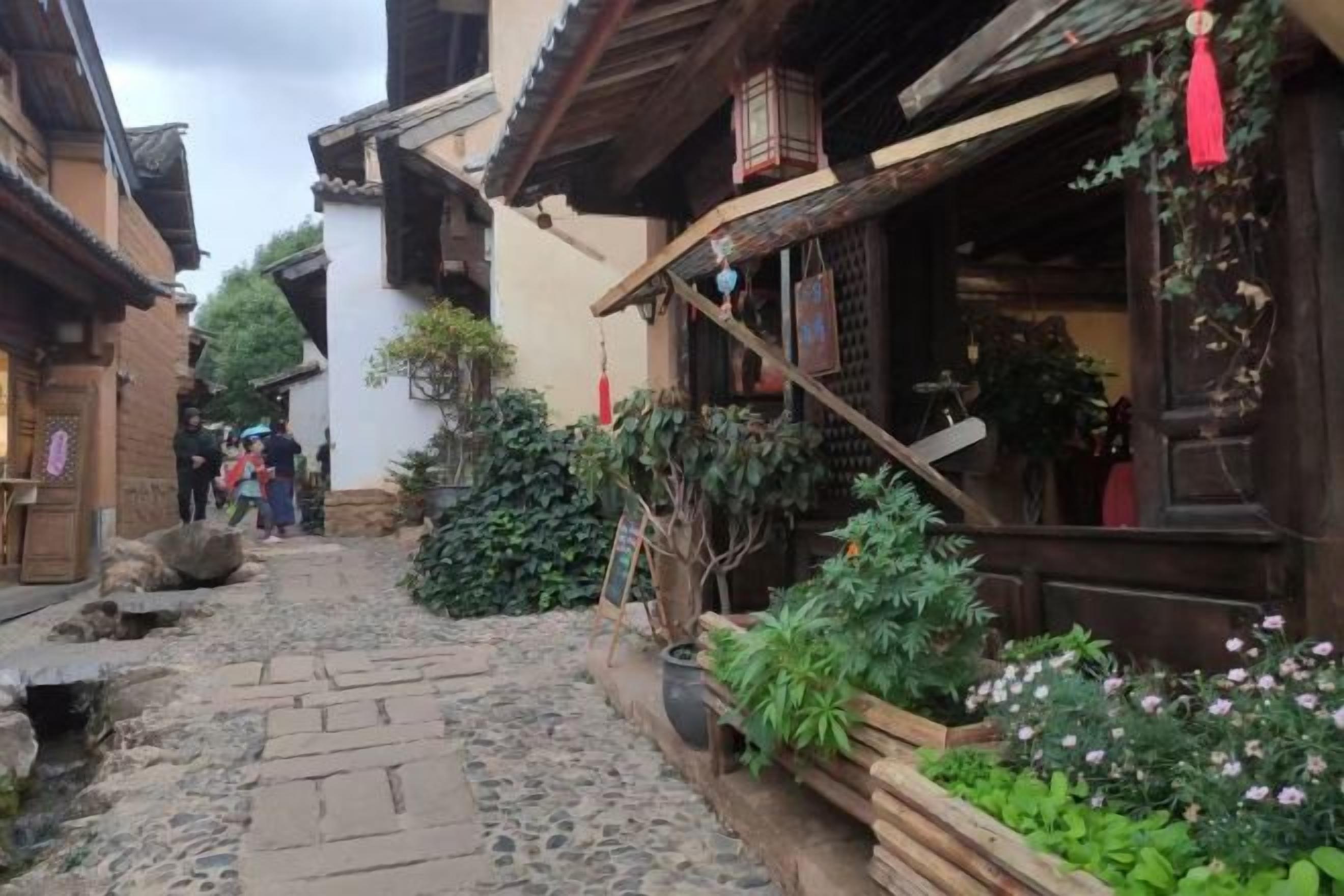 A narrow cobblestone alley with traditional wooden buildings, some with visible signage and plants.