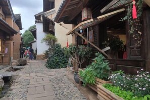 A narrow cobblestone alley with traditional wooden buildings, some with visible signage and plants.