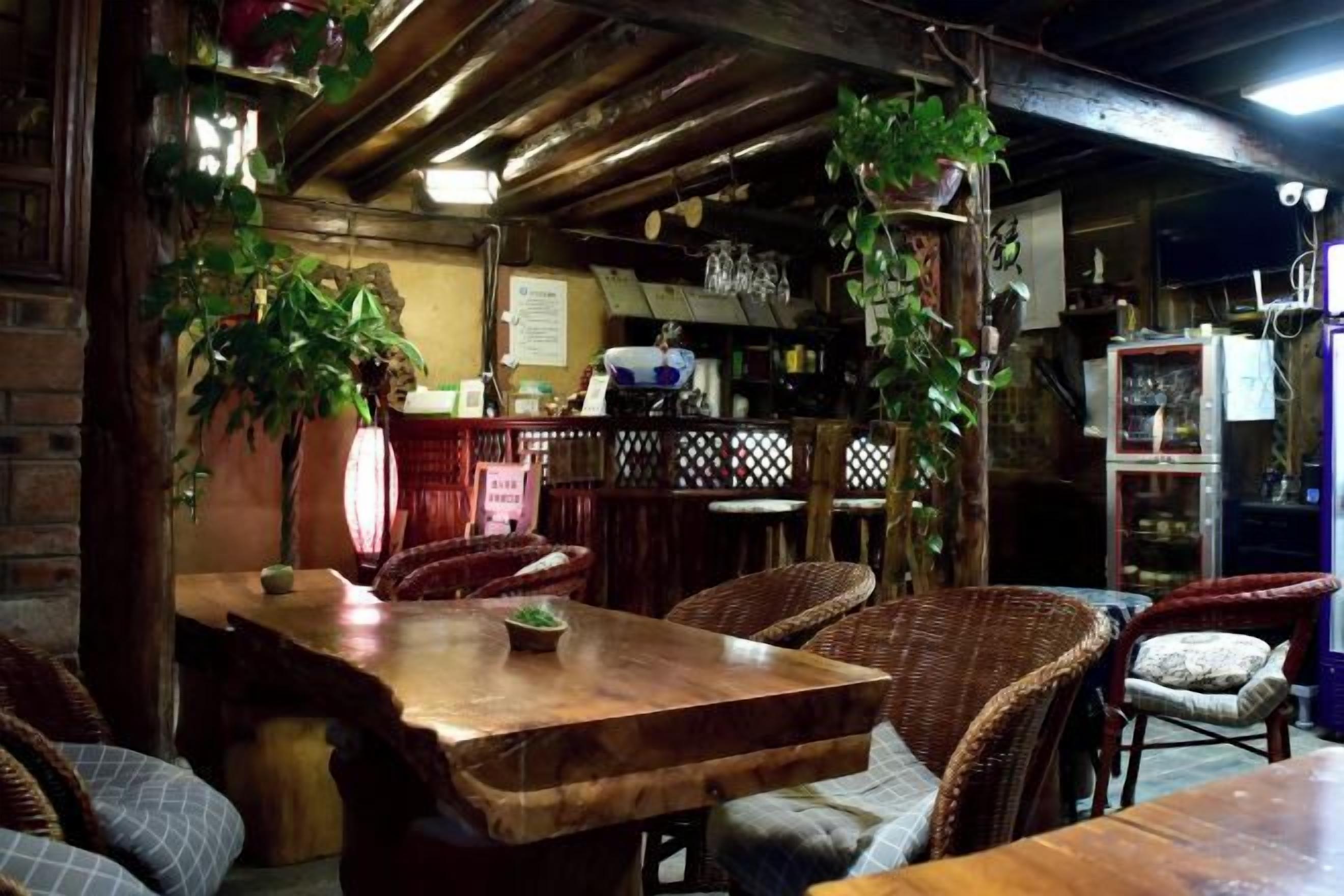Un comedor rústico con una mesa de madera y sillas de mimbre, rodeado de plantas colgantes y una pared de ladrillo.