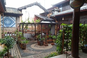 Un cortile con una pergola in legno, piante in vaso e pavimento in piastrelle tradizionali.