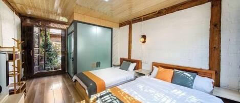A hotel room with wooden flooring, a large bed with multiple pillows, a nightstand, and a window with a view of greenery.