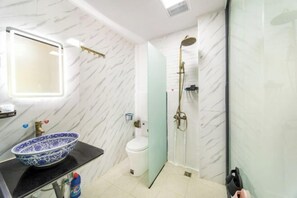 Une salle de bain avec un mur en marbre, un lavabo en forme de bol aux couleurs bleu et blanc, des toilettes et une douche à parois de verre.