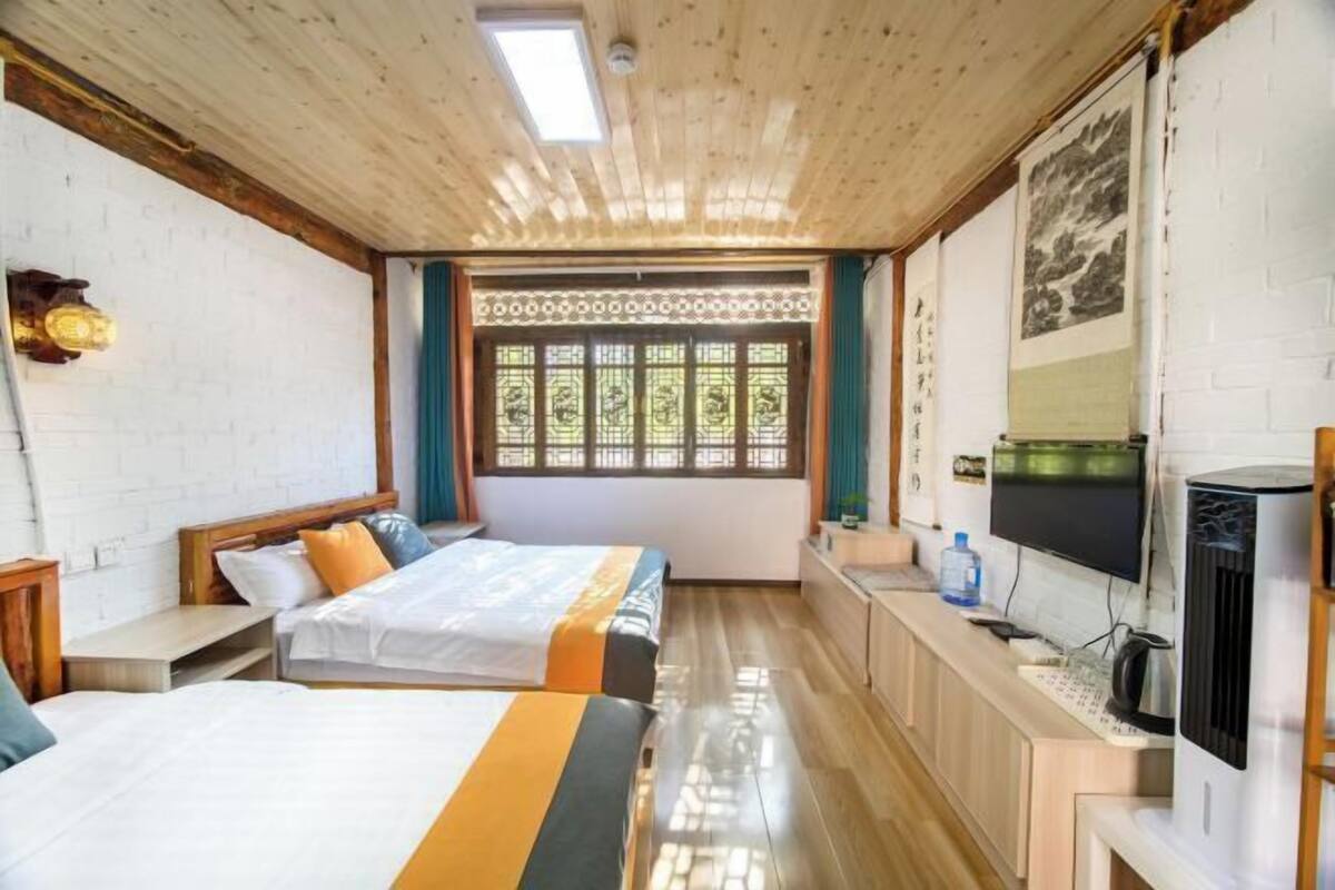Ein Hotelzimmer mit zwei Betten, einem Fernseher, einer Heizung und einem Fenster mit dekorativen Läden.