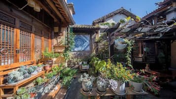 A traditional Japanese courtyard with potted plants, a tiled floor, and wooden structures.
