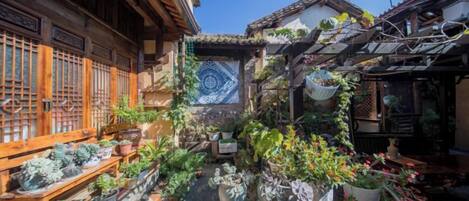 A traditional Japanese courtyard with potted plants, a tiled floor, and wooden structures.
