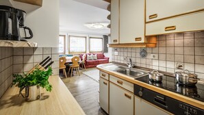 A kitchen with a stove, sink, and cabinets. There is a plant on the counter and a red couch in the background.