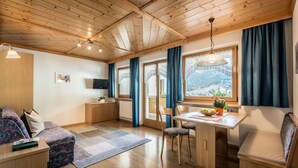 A cozy room with a wooden ceiling, a dining table with chairs, a sofa, and a TV on the wall.