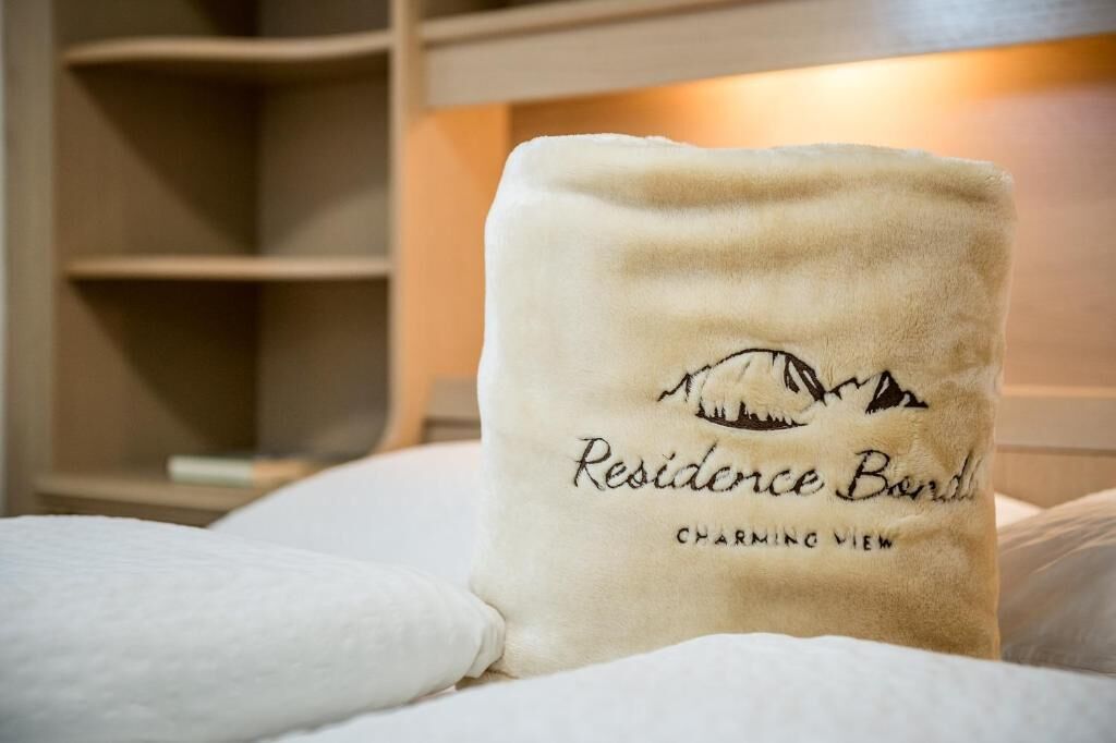 Une serviette blanche ornée des inscriptions « Residence Bond » et « Charming View », posée sur un lit recouvert de draps blancs.