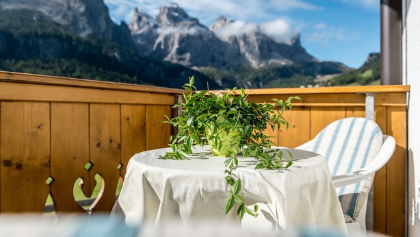 A table with a white tablecloth, a potted plant, and a striped chair. A wooden wall and a mountain view are in the background.