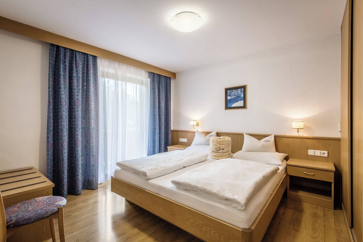 Habitació d'hotel amb llit de fusta, dues taules de nit, un escriptori petit i una cadira.