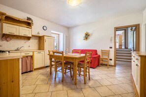A kitchen with wooden cabinets, a dining table with chairs, a red sofa, and a staircase leading to another level.