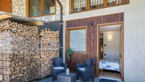 A patio with two wicker chairs, a small table, and a stack of firewood. - Holiday Apartment "Agritur Piazera Con Terrazzo" with Mountain View (Ronzo Chienis)