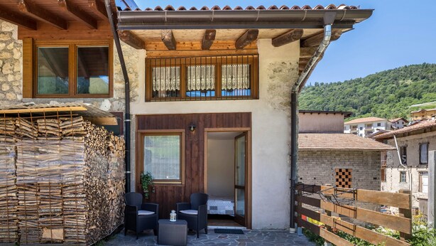 A two-story building with a stone facade, a wooden balcony, and a view of a hillside. - Holiday Apartment "Agritur Piazera Con Terrazzo" with Mountain View (Ronzo Chienis)