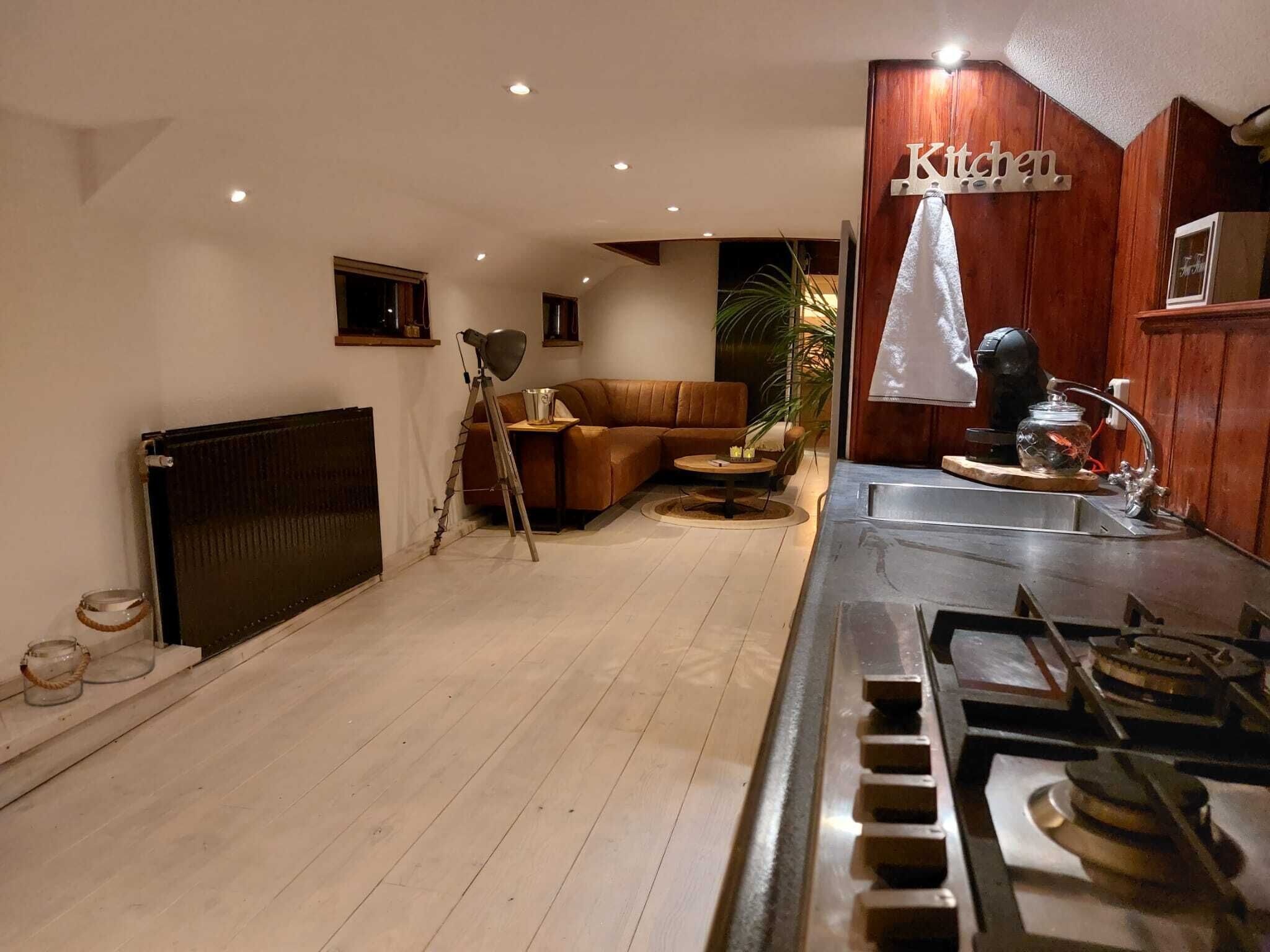 A modern kitchen with a wooden cabinet, a stove, and a dining area with a brown sofa and a small table.