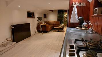 A modern kitchen with a wooden cabinet, a stove, and a dining area with a brown sofa and a small table.