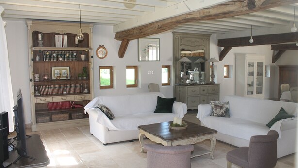 A spacious living room with two white sofas, a coffee table, and a television. There is a wooden bookshelf and a kitchen area in the background. - Maison Solognote au Coeur des Châteaux de la Loire (Tour en Sologne)