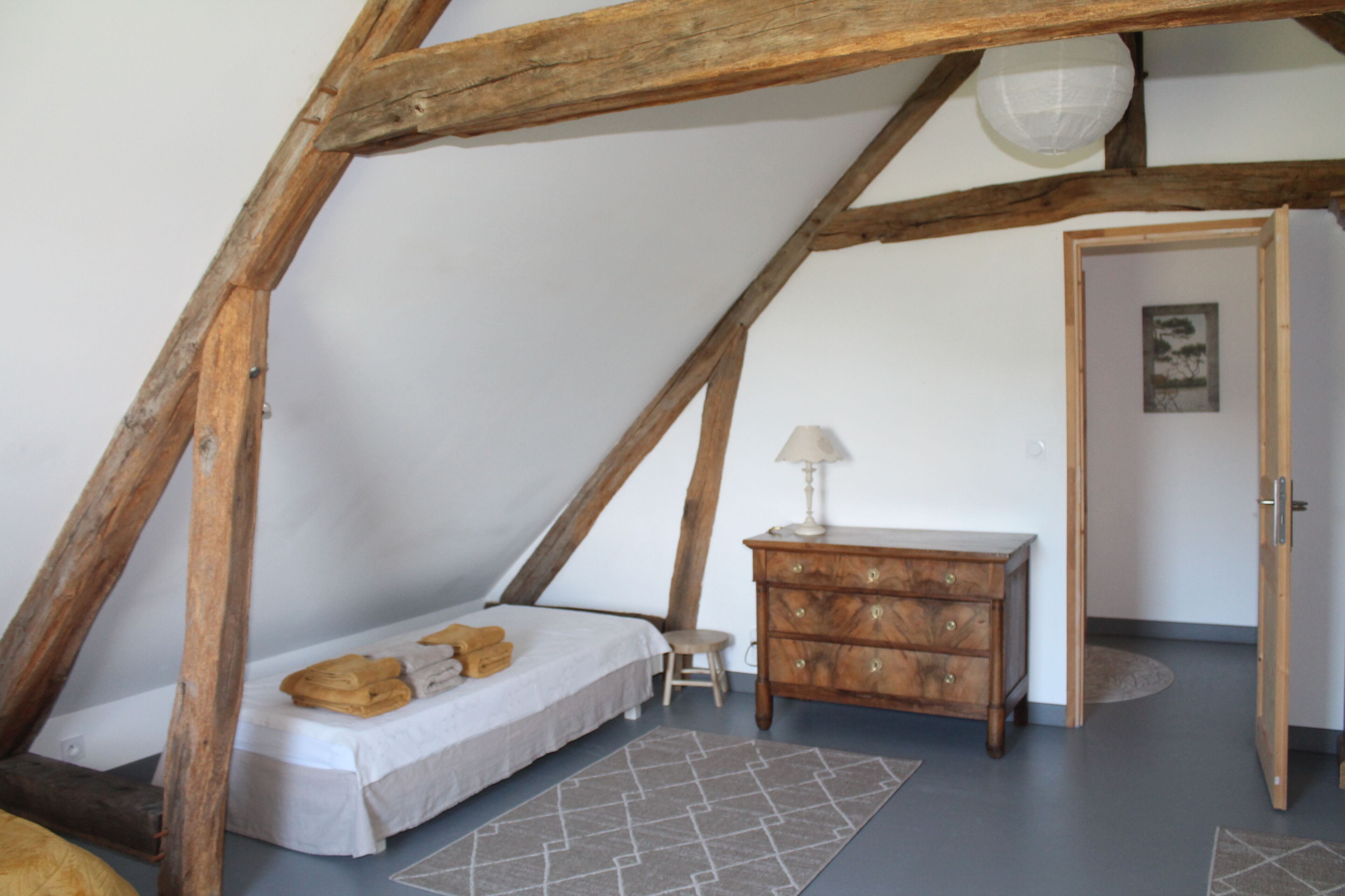 Een slaapkamer met een schuine kap, een bed met handdoeken, een houten dressoir en een klein krukje.