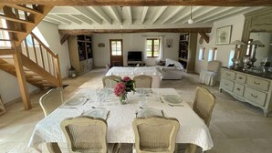 A dining area with a wooden staircase, a white table set for four, and a cozy living room in the background. - Maison Solognote au Coeur des Châteaux de la Loire (Tour en Sologne)