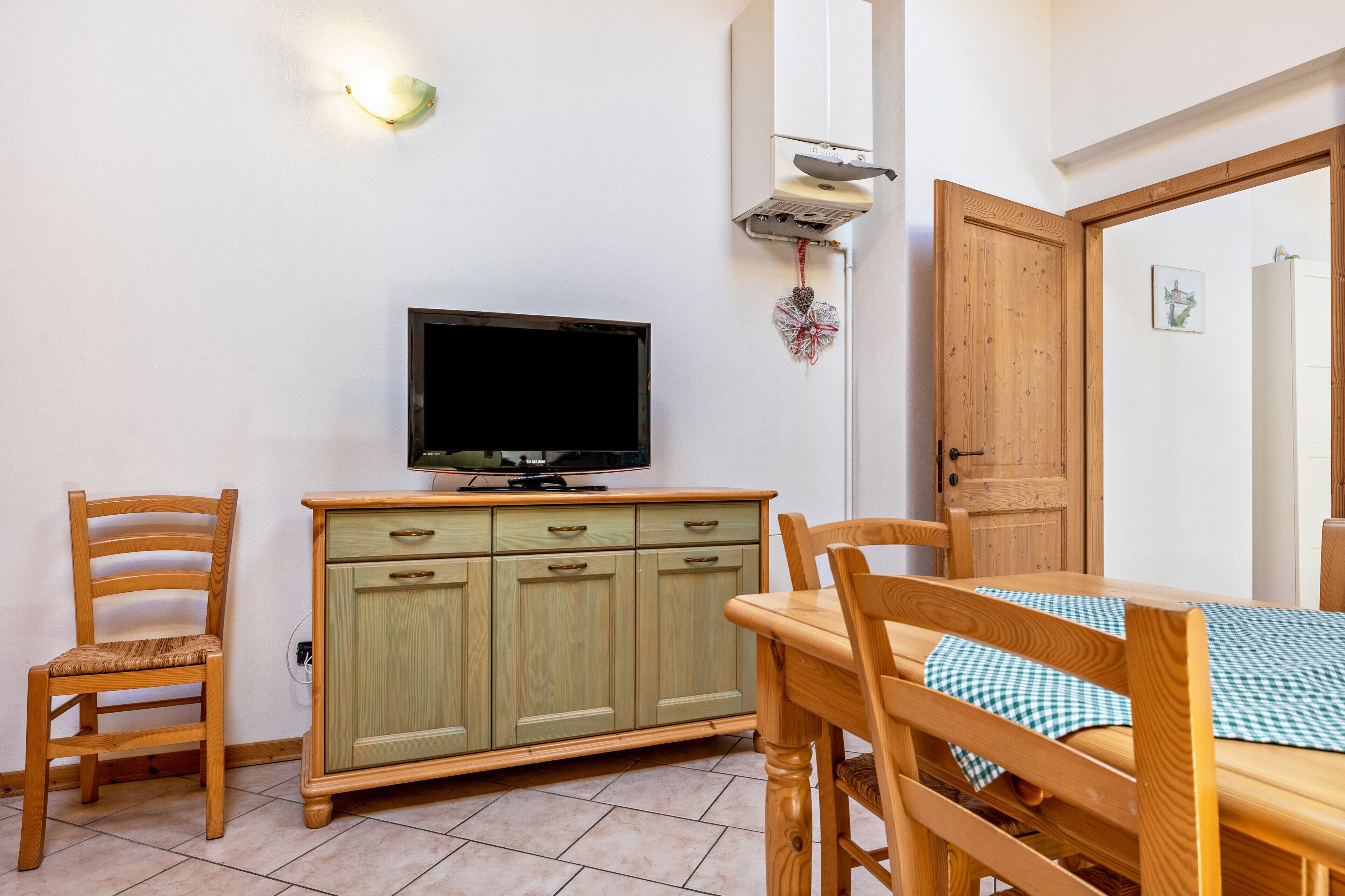 A room with a wooden dining table, two chairs, a television on a cabinet, and a door.
