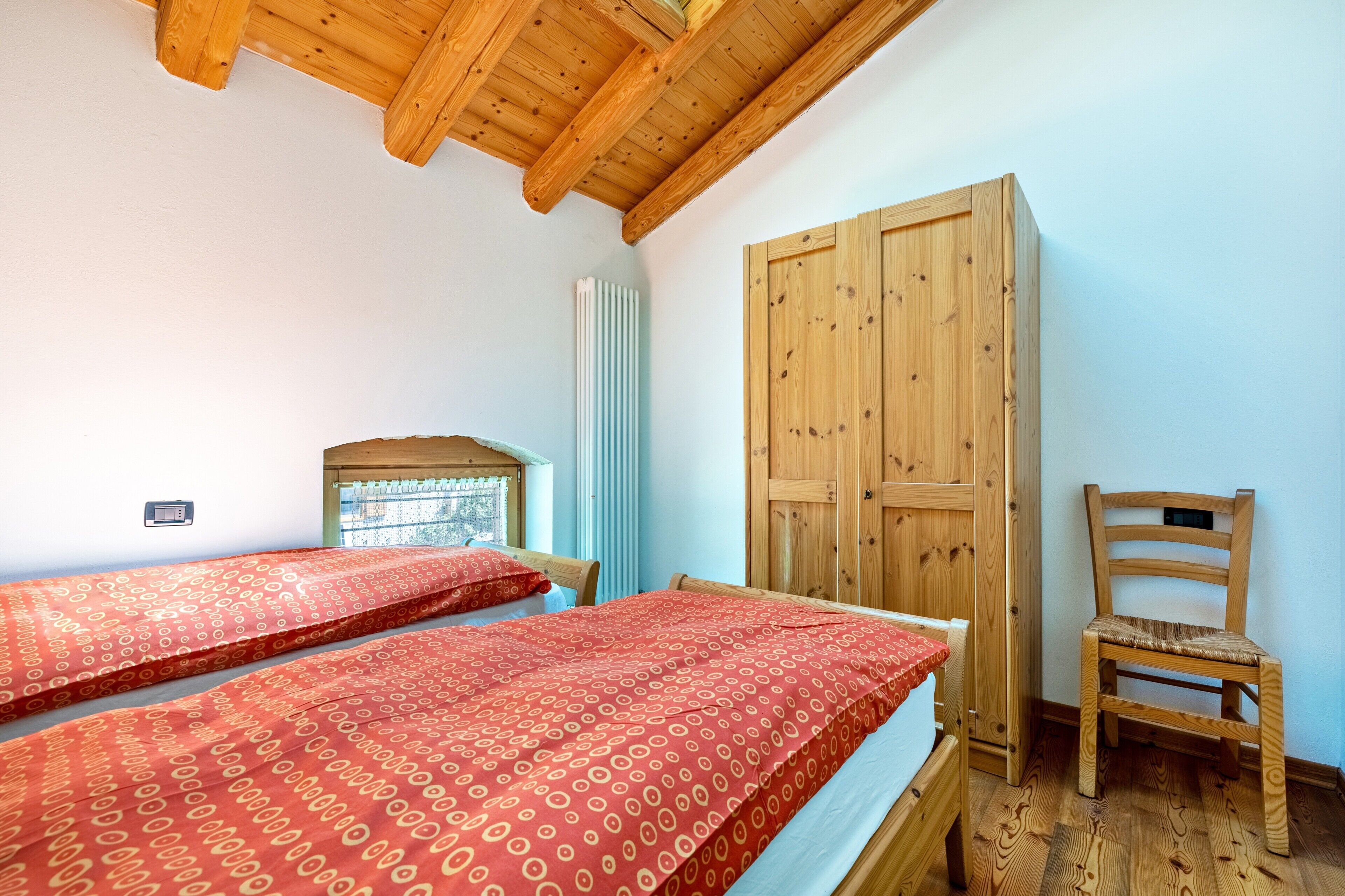 A room with two beds, a wooden wardrobe, a chair, and a radiator.