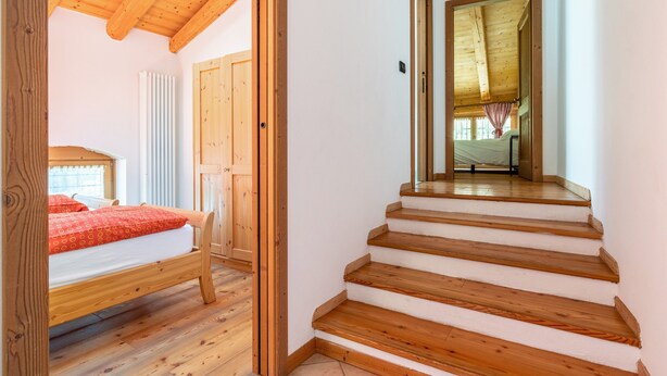 A bedroom with a wooden bed, a staircase, and a view into another room.