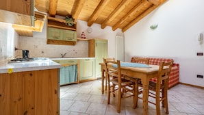 A kitchen with wooden cabinets, a dining table with chairs, a red plaid sofa, and a clock on the wall.