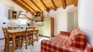 A kitchen with wooden beams, a dining table with chairs, a red plaid sofa, and a radiator.