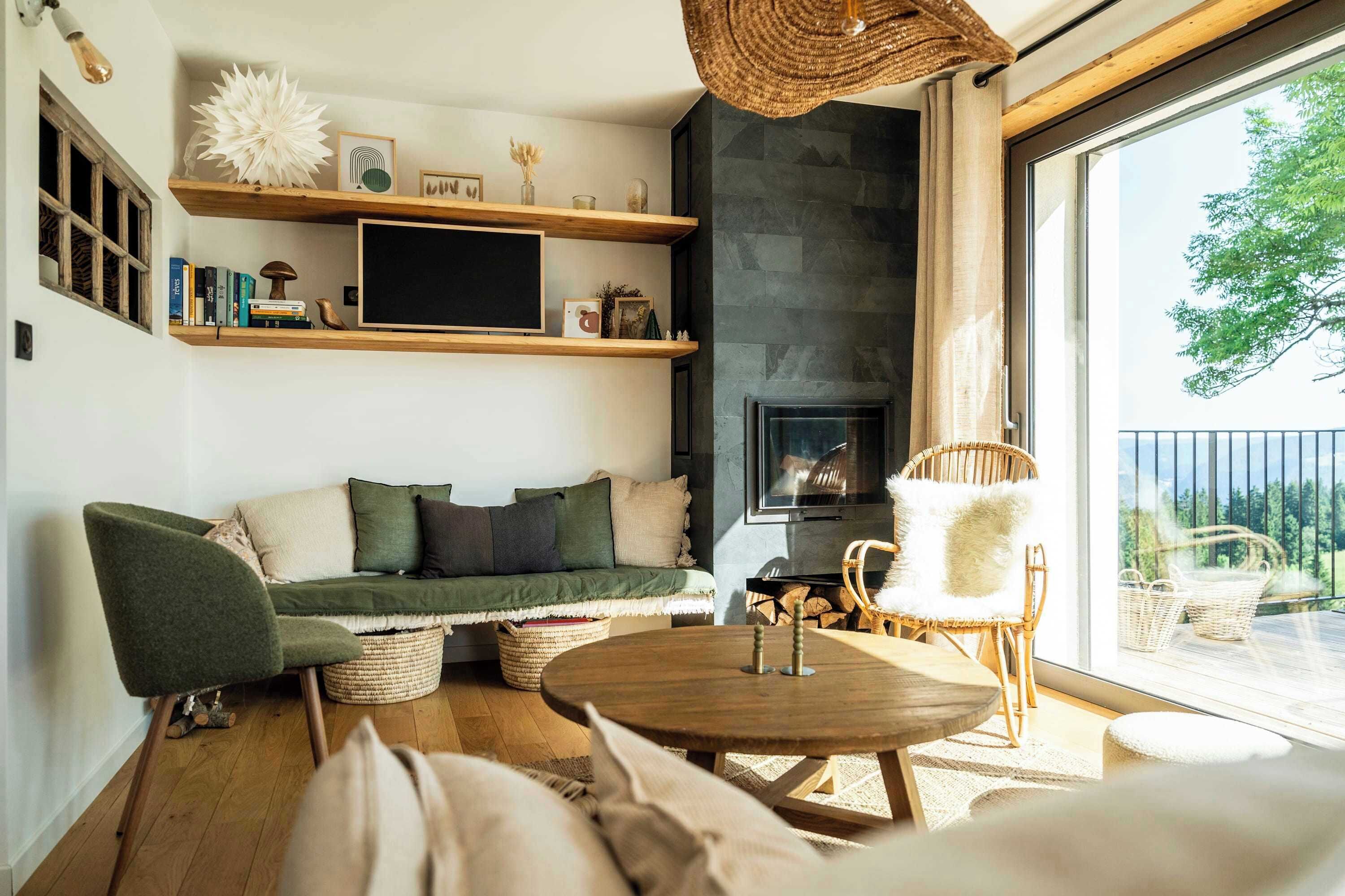 Een gezellige woonkamer met een open haard, houten planken en een groot raam met uitzicht op een balkon.