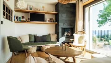 A cozy living room with a fireplace, wooden shelves, and a large window overlooking a balcony.