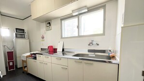 A compact kitchen with white cabinets, a stainless steel sink, a microwave, and a red kettle. - chidoriasahinoie (Osaka)