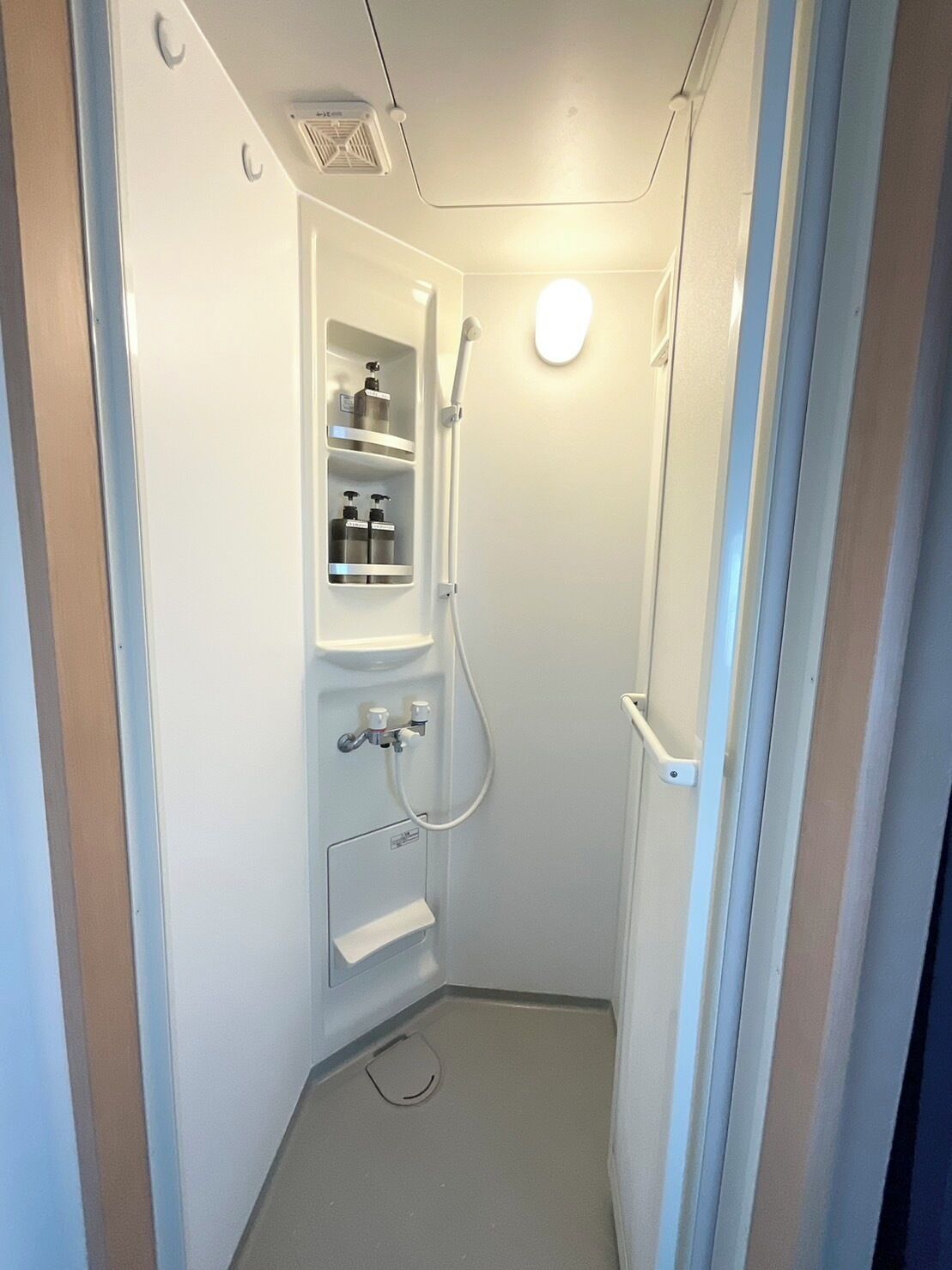 A small, white, enclosed shower area with a built-in shelf holding toiletries.