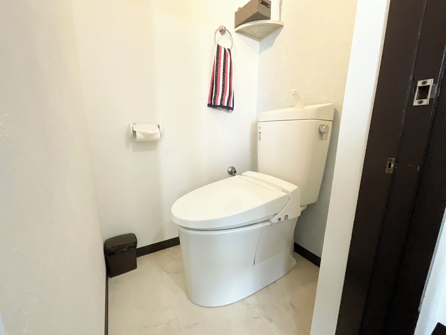 A small, clean bathroom with a white toilet, a towel rack with a striped towel, and a toilet paper holder.
