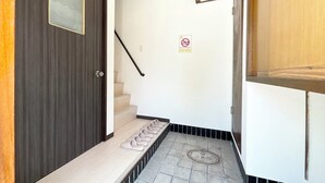 A narrow hallway with a dark wooden door, a staircase with beige steps, and a tiled floor. - chidoriasahinoie (Osaka)