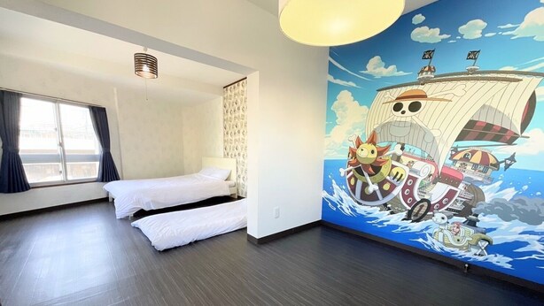 A hotel room with two single beds, a large window with curtains, a ceiling fan, and a mural of a ship with characters. - chidoriasahinoie (Osaka)