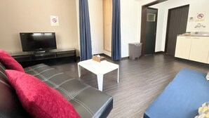 A modern living room with a flat-screen TV, a sofa with red cushions, a small white table, and a kitchenette area with a sink and cabinets. - chidoriasahinoie (Osaka)