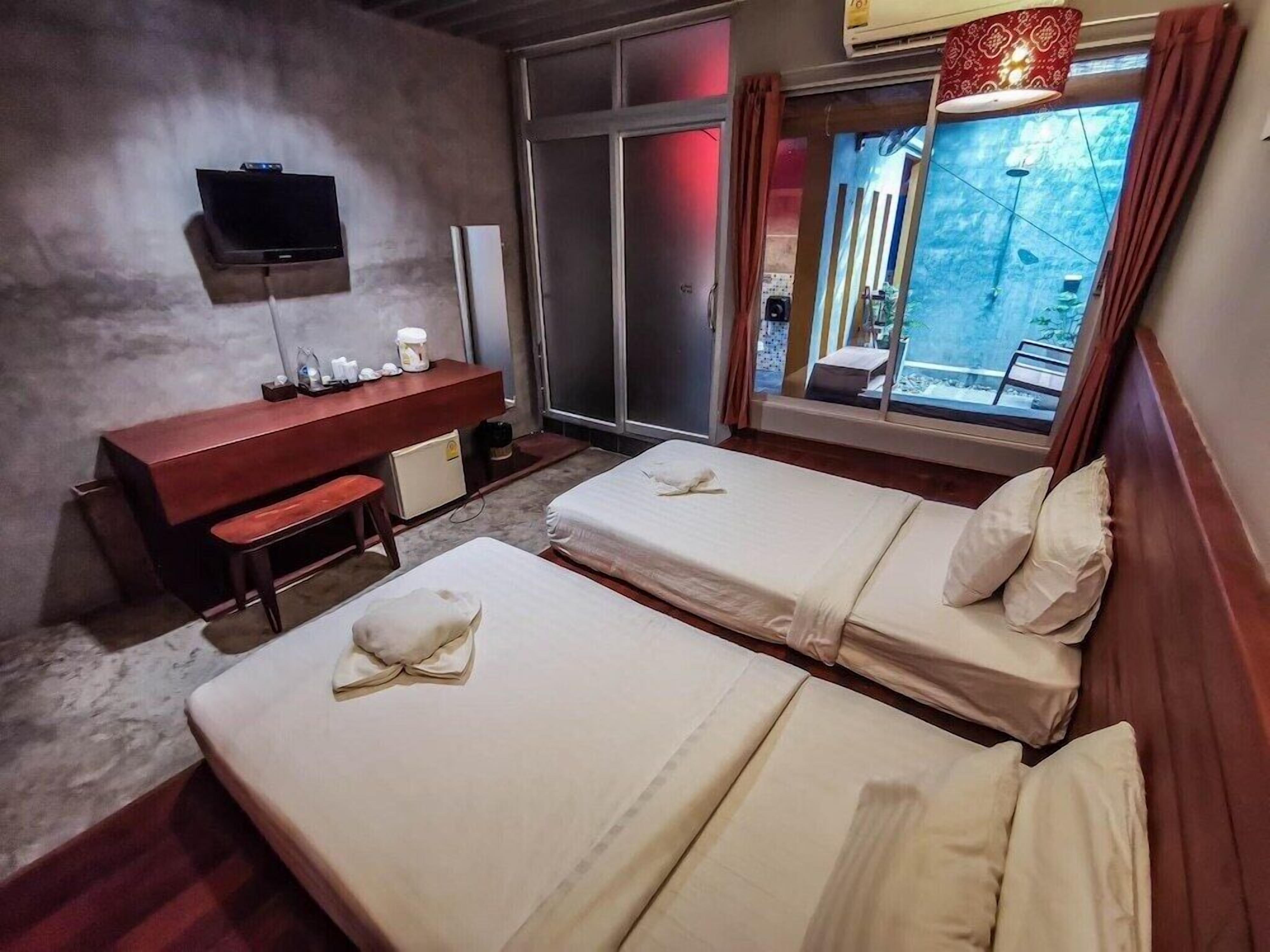 A hotel room with two beds, a desk, a TV, and a window with curtains.