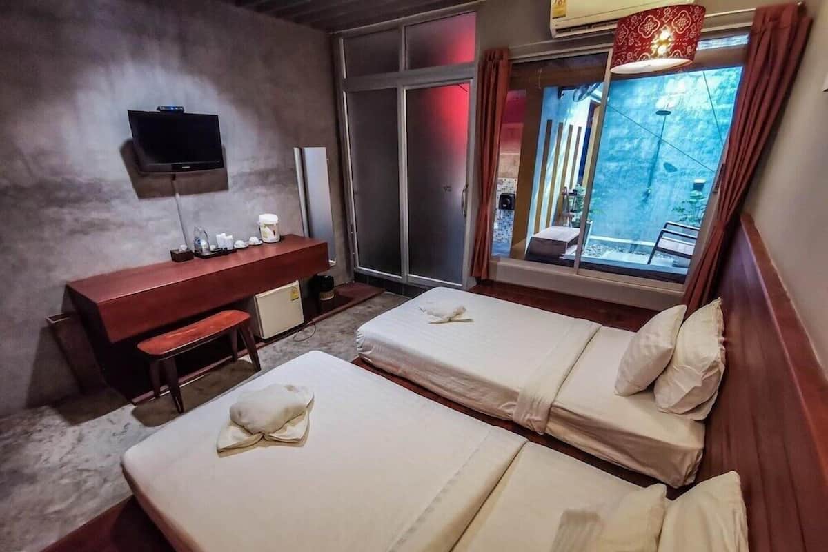 A hotel room with two beds, a desk, a TV, and a window with curtains.
