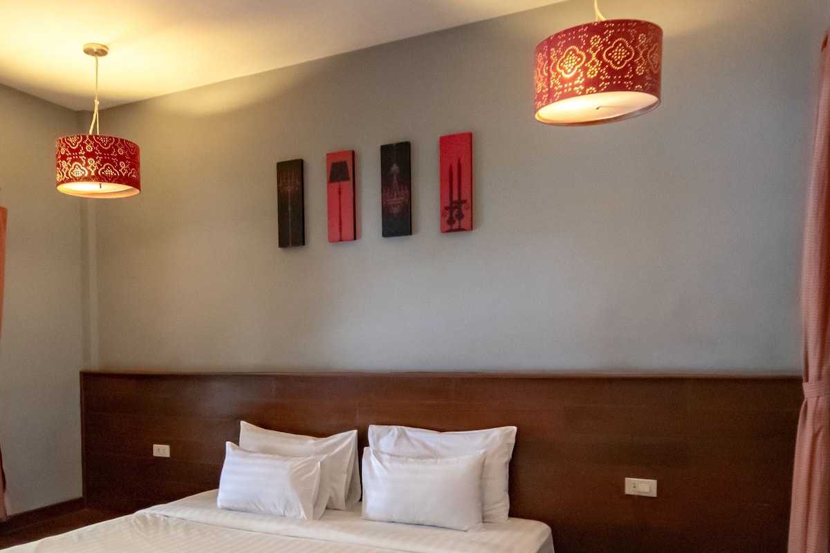 A hotel room with a large bed, two hanging lamps, and four wall-mounted artworks.