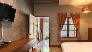 Een hotelkamer met een bed, een aan de muur bevestigde televisie, een houten bankje en een raam met gordijnen.