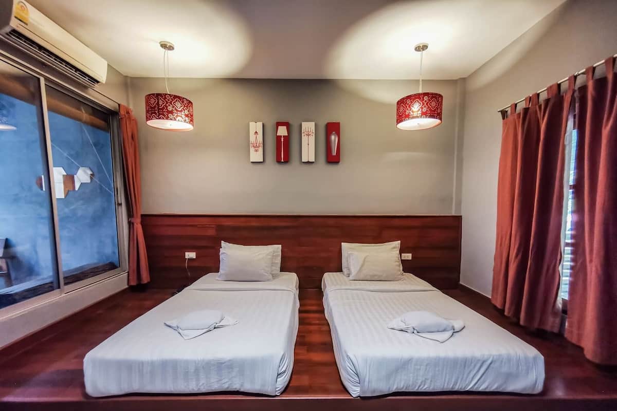 A hotel room with two beds, a large window, and a wall-mounted air conditioner.
