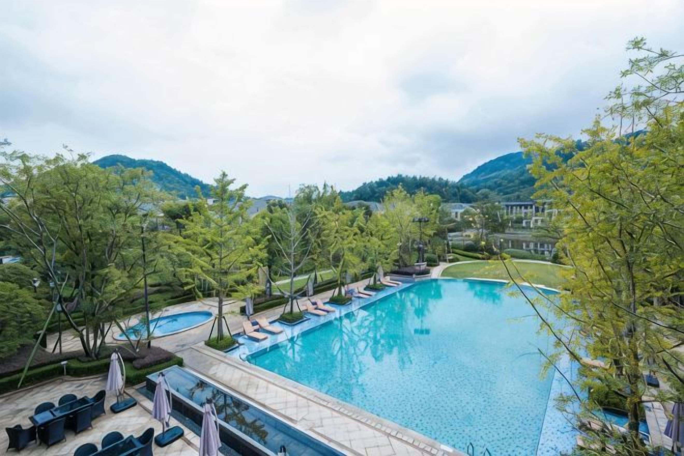 A swimming pool with lounge chairs and umbrellas, surrounded by trees and hills.