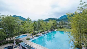 A swimming pool with lounge chairs and umbrellas, surrounded by trees and hills.