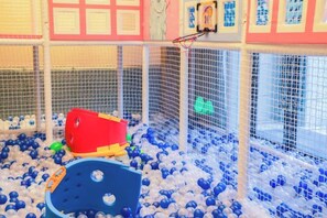 Un área de juegos con piscina de pelotas, un módulo de juegos rojo y amarillo, y un aro de baloncesto.