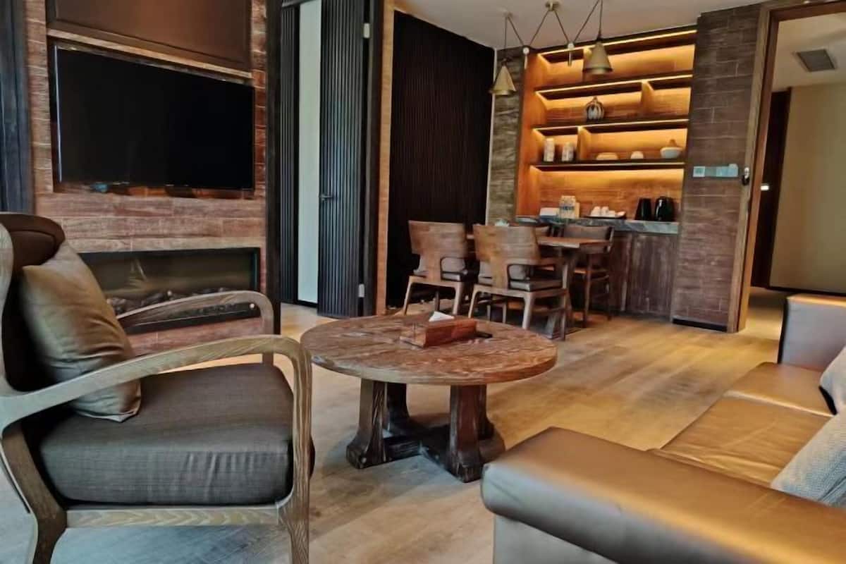 A modern living room with a fireplace, a round wooden coffee table, leather sofas, and a kitchen area with built-in shelves.
