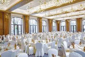 Une salle de banquet avec des tables rondes, des chaises blanches et des lustres.