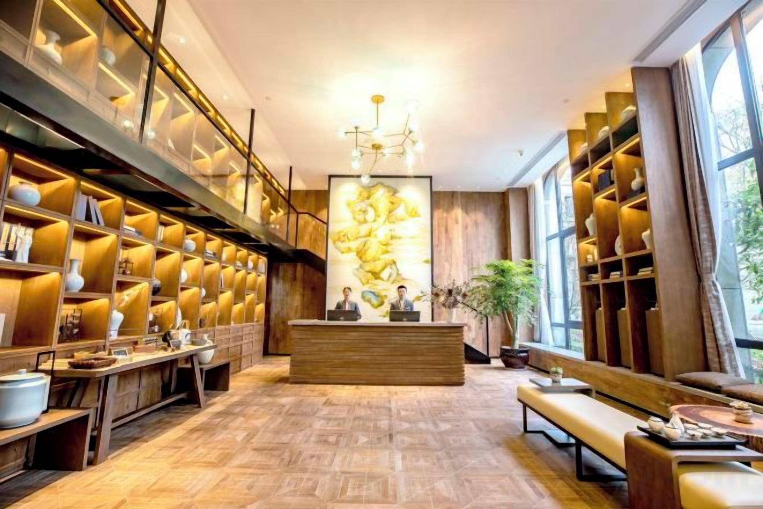 A hotel lobby with a reception desk, wooden shelving with vases, and a large window.