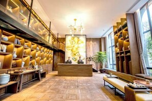 A hotel lobby with a reception desk, wooden shelving with vases, and a large window. - Azure Reserve Deqing (DEQING)