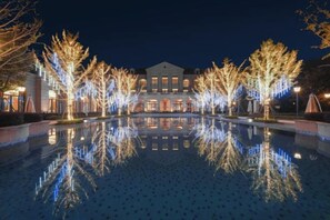 A nighttime view of a hotel with a reflective pool, trees with lights, and a building with multiple windows. - Azure Reserve Deqing (DEQING)